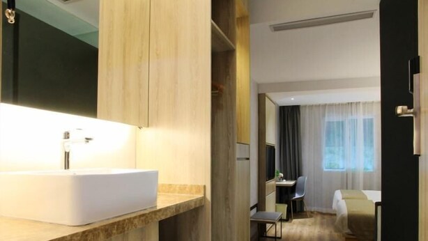 A modern hotel room with a large bathroom vanity, a desk, a chair, and a bed. - Vatica Fuzhou West Second Ring Road Xihu Park Hote (Fuzhou)