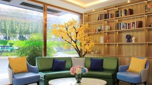 A modern living room with a green sofa, two armchairs, a coffee table, and a bookshelf filled with books and decorative items. - Vatica Fuzhou West Second Ring Road Xihu Park Hote (Fuzhou)
