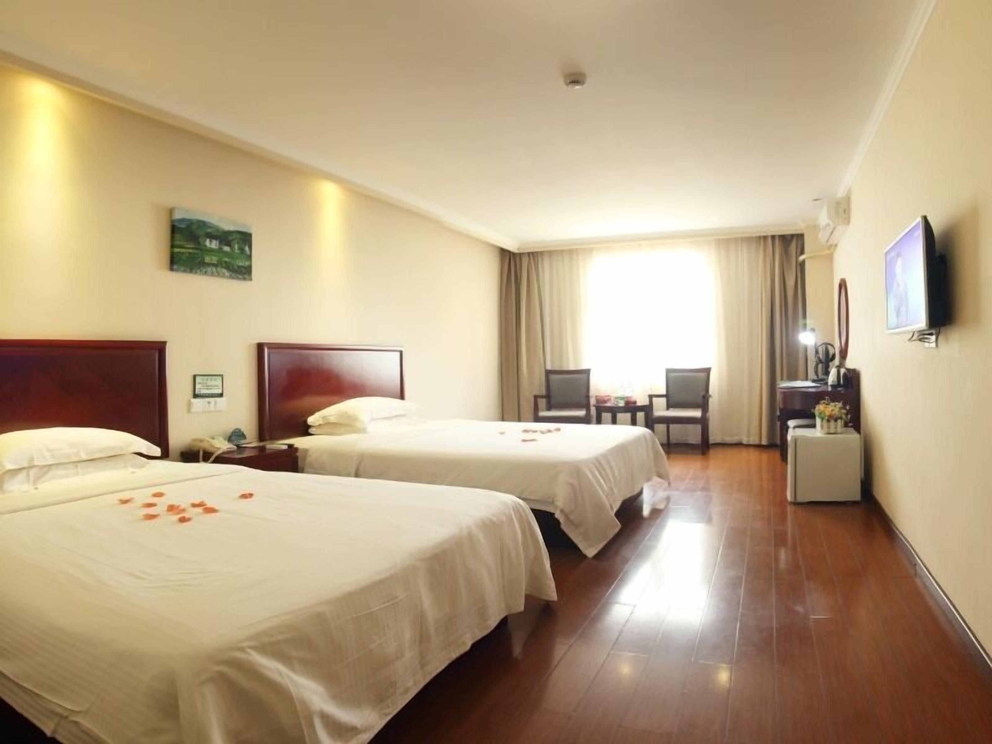 A hotel room with two beds, a desk, a chair, a television, and a painting on the wall.