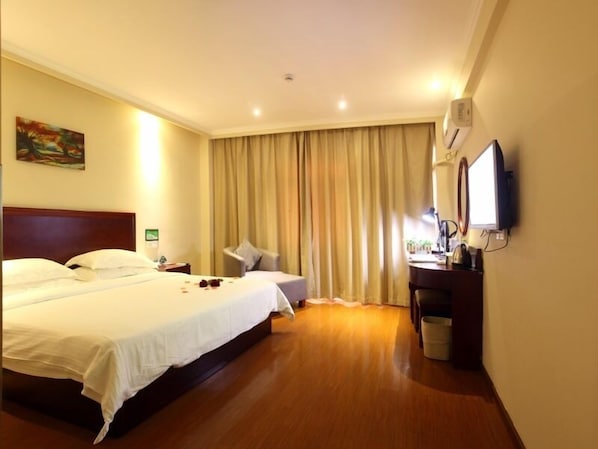 A hotel room with a large bed, a desk with a chair, a television, and a window with curtains.