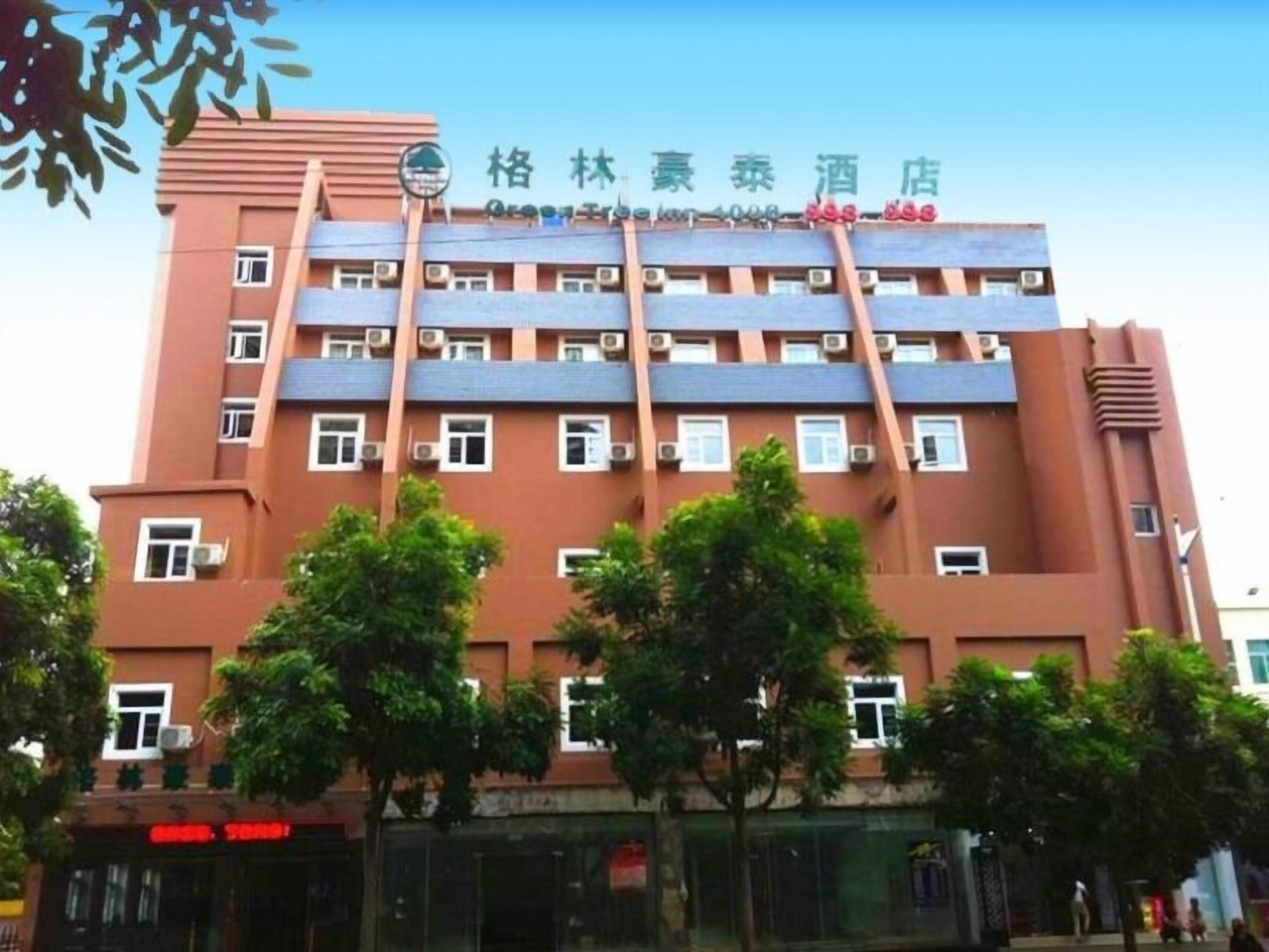 A multi-story hotel with a red facade, multiple air conditioning units, and a sign indicating the name and contact number.