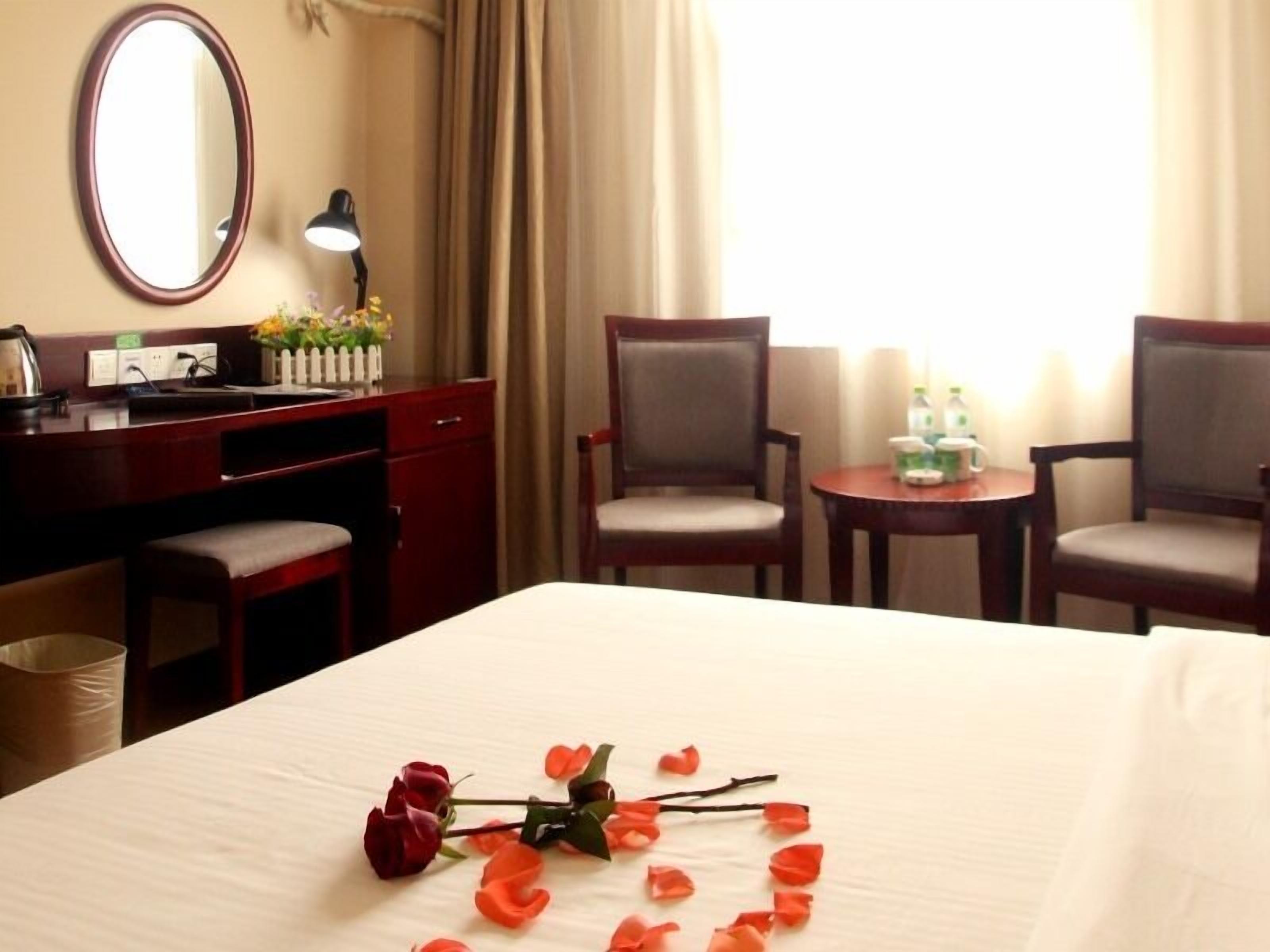 A hotel room with a bed, two chairs, a desk, a mirror, a lamp, and a window with curtains.