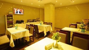 A dining area with multiple tables and chairs, a television mounted on the wall, and a buffet setup. - GreenTree Inn Haikou Longhua District Guomao Hotel (Haikou)