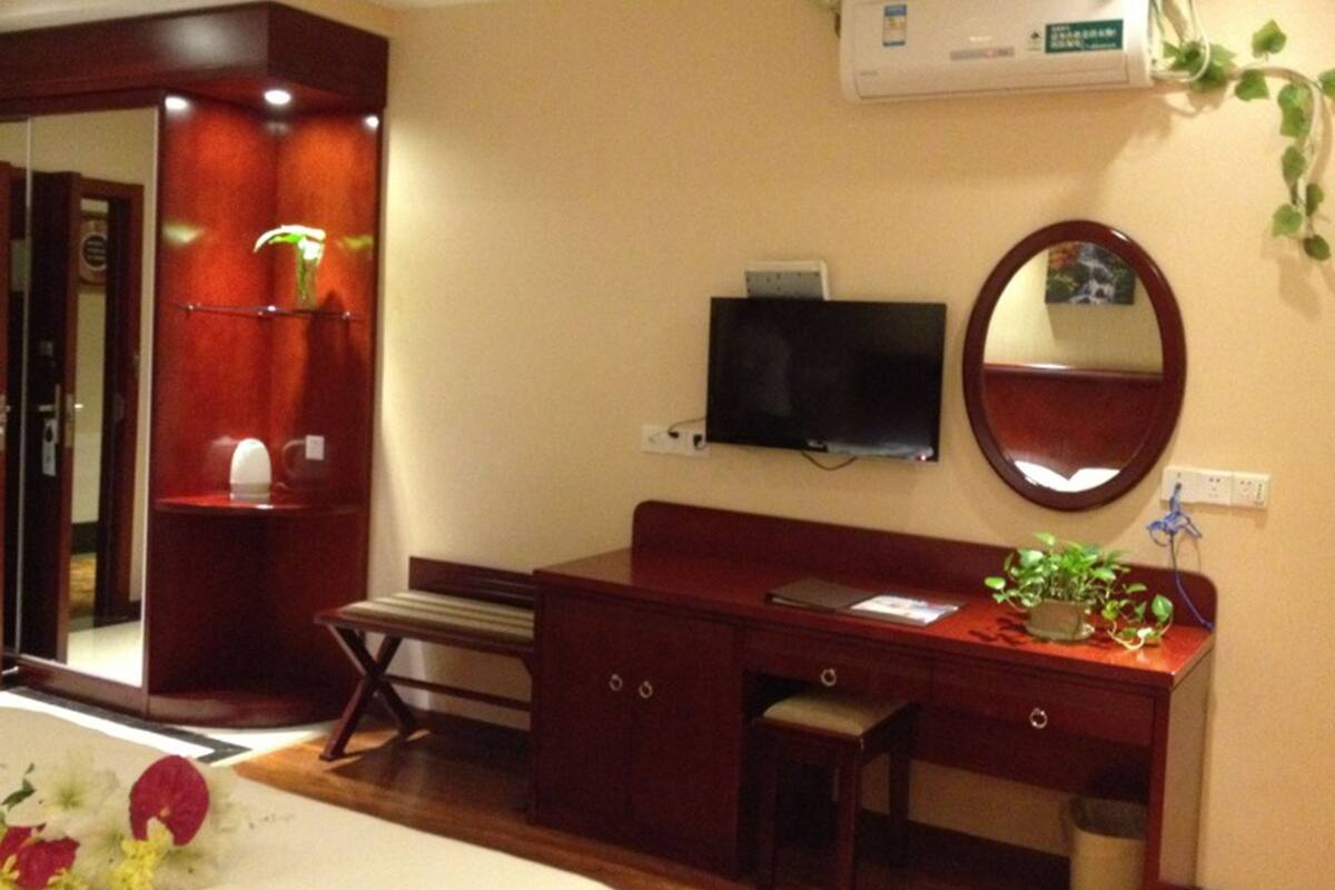 Habitación de hotel con un escritorio de madera, un televisor montado en la pared, un espejo y un equipo de aire acondicionado.
