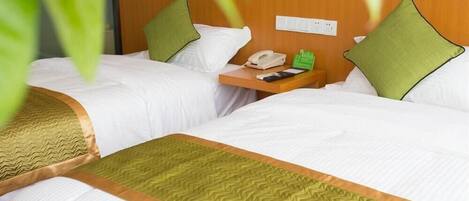A hotel room with two beds, each with white bedding and green pillows. There is a wooden nightstand with a telephone and a green bottle.
