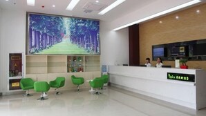 A modern reception area with a large digital screen displaying a forest path, green chairs, a reception desk, and a wooden accent wall. - Vatica Lianyungang Zhongyin Mingdu Hotel (Lianyungang)