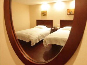 A mirrored view of a hotel room with two beds, a nightstand, and a wall-mounted lamp. - GreenTree Inn YangZhou West KaiFa Road Baolong Square Express Hotel (Yangzhou)
