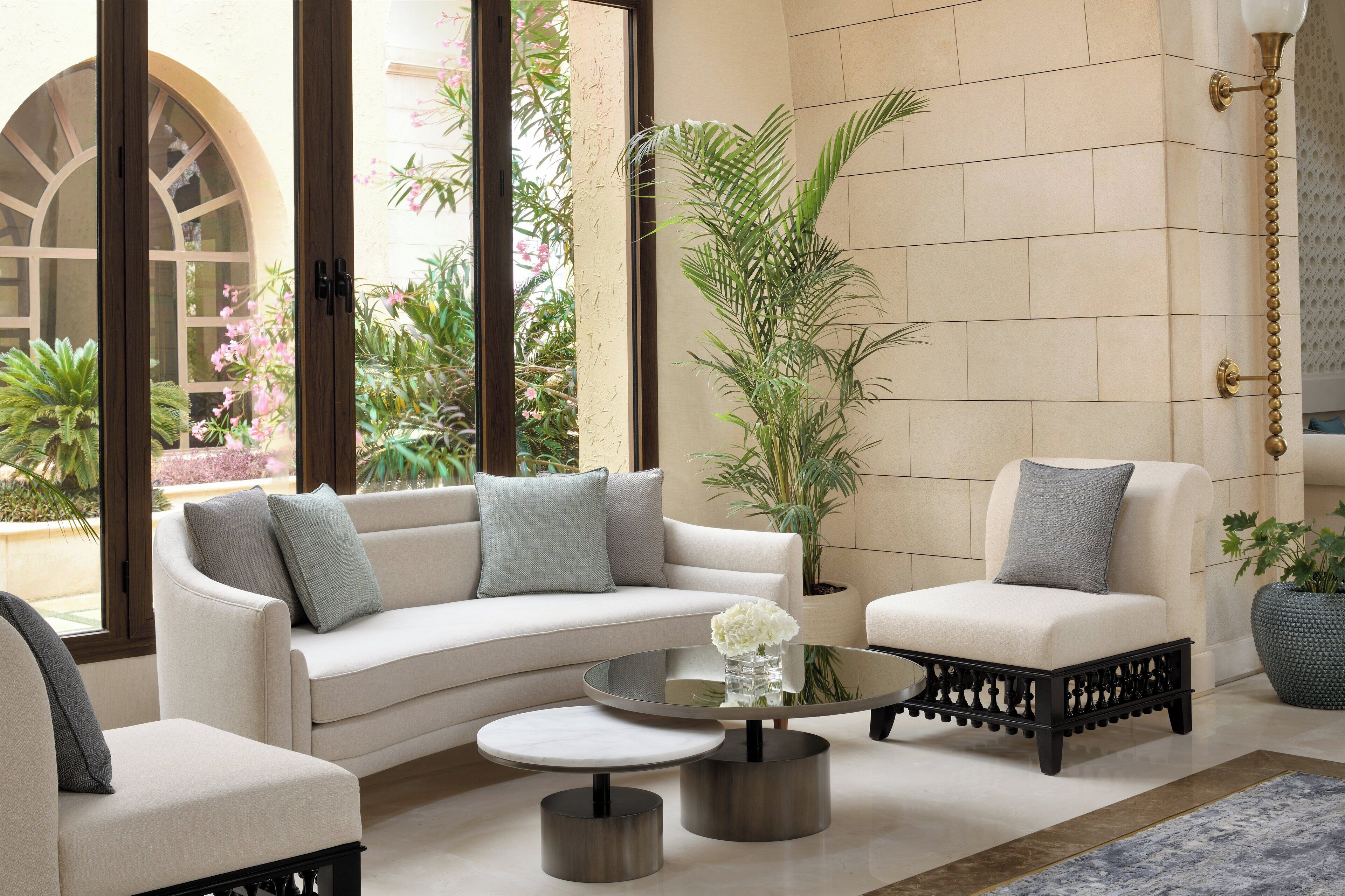 A modern living room with a white sofa, two armchairs, a coffee table, and a large window with a view of greenery.