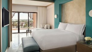 A hotel room with a large bed, a small table with a vase of flowers, a bench, and a view of the outdoors through a sliding door.