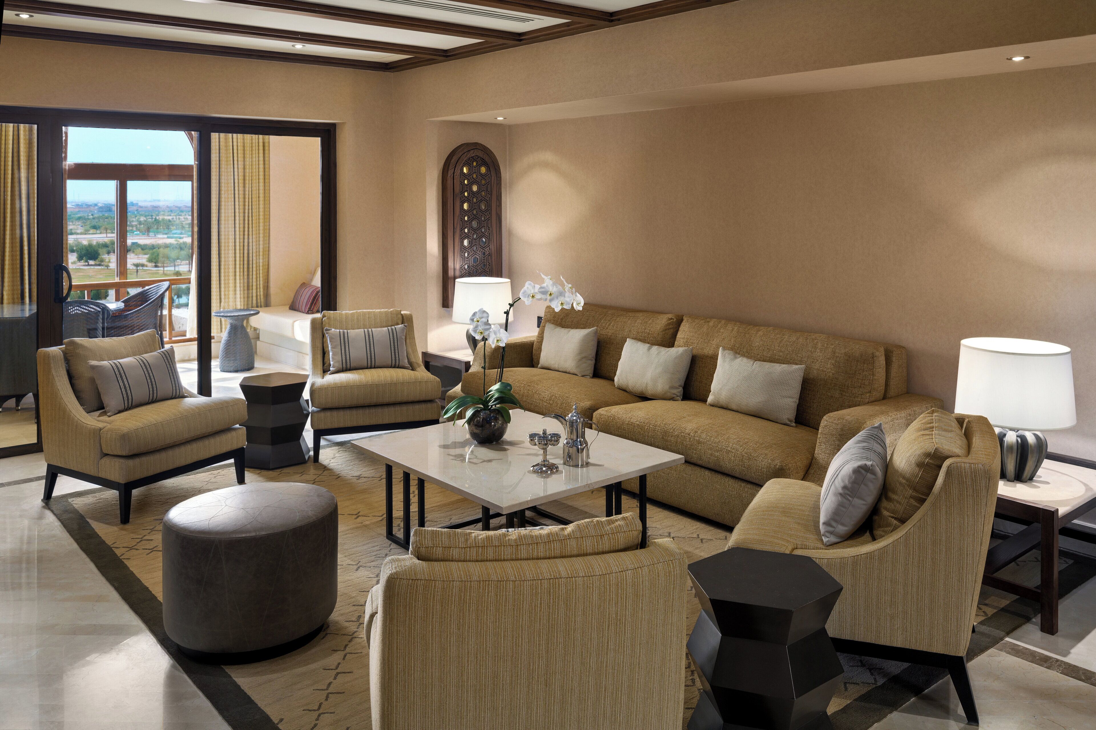 A spacious living room with a large sofa, armchairs, a coffee table, and a view through a large window.
