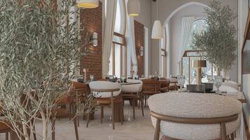 Un restaurant avec des tables rondes, des chaises et des oliviers.