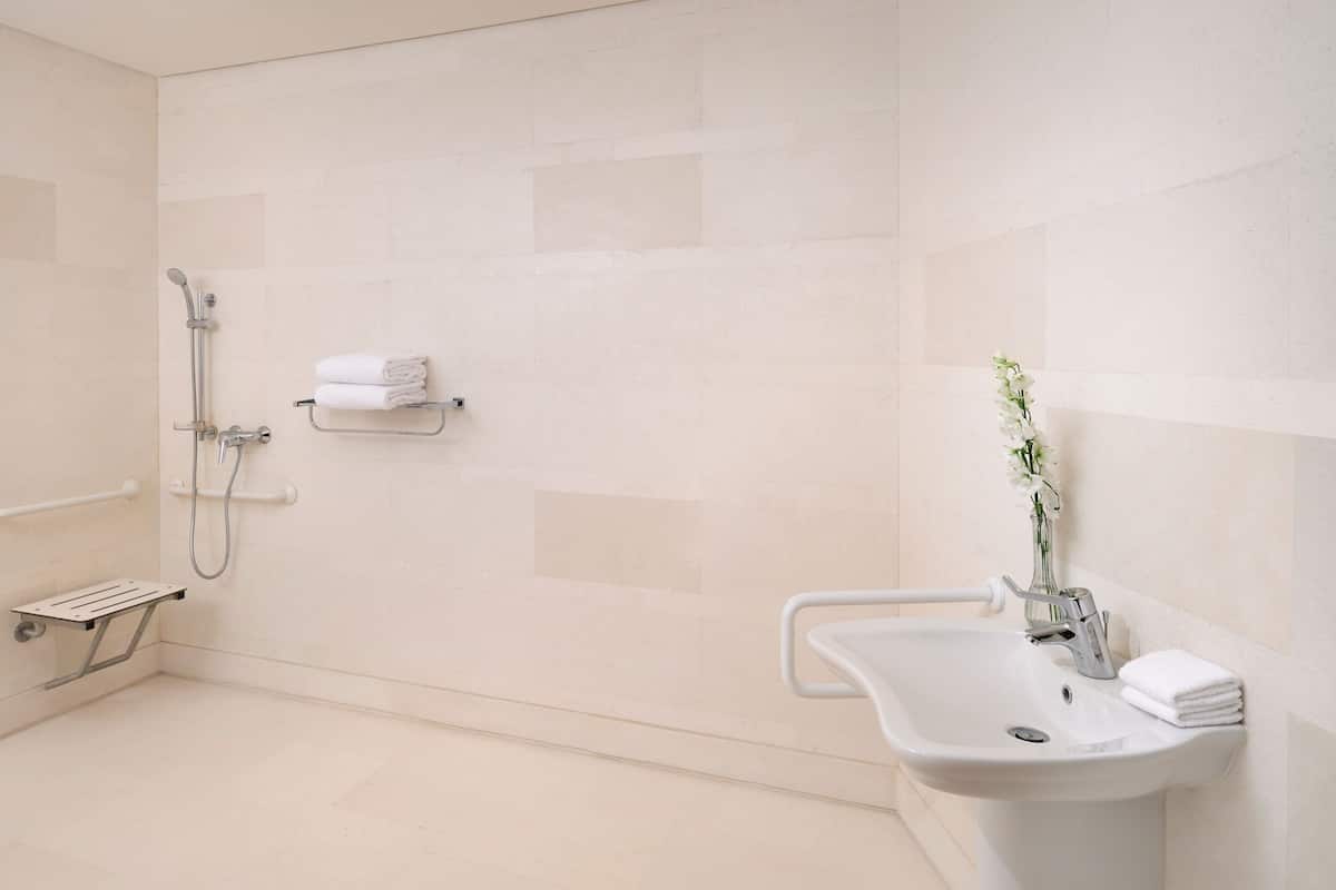 A modern bathroom with a shower, a sink, and a small shelf with towels.