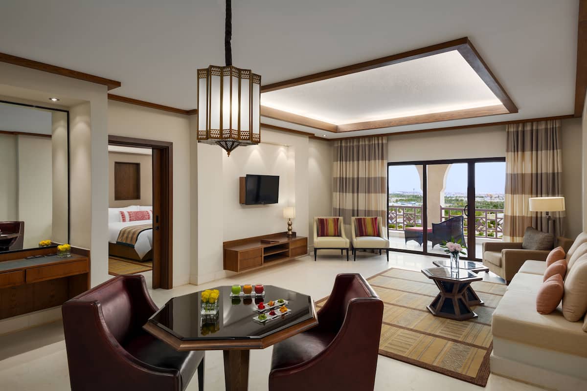 A modern hotel room with a dining area, a sofa, and a television.