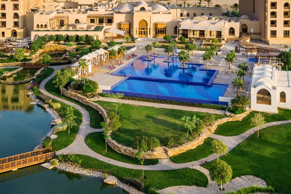 A resort with a large central pool, landscaped gardens, and a bridge over a body of water.