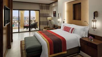 A hotel room with a large bed, a flat-screen TV, a balcony with a view, and a wooden headboard.