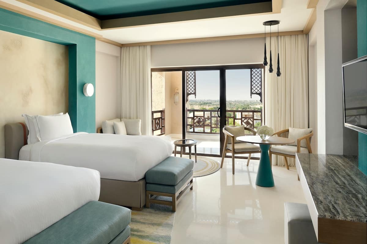 A hotel room with two beds, a balcony with a table and chairs, and a TV.