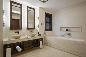 A modern bathroom with a large bathtub, two sinks, and a vanity with a mirror.