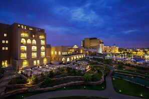 A hotel with multiple floors, outdoor seating areas, and a landscaped garden with a pool.