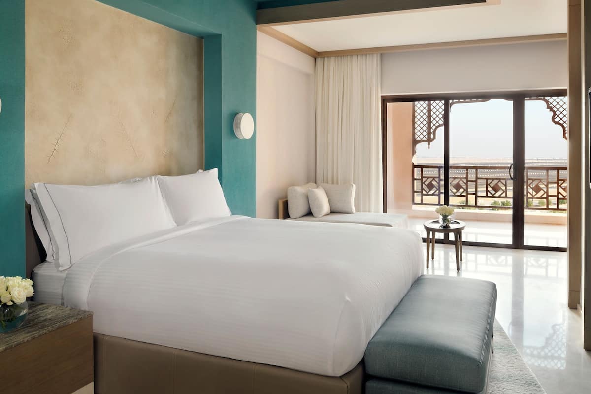 A hotel room with a large bed, a small table with a vase of flowers, and a balcony with a view.