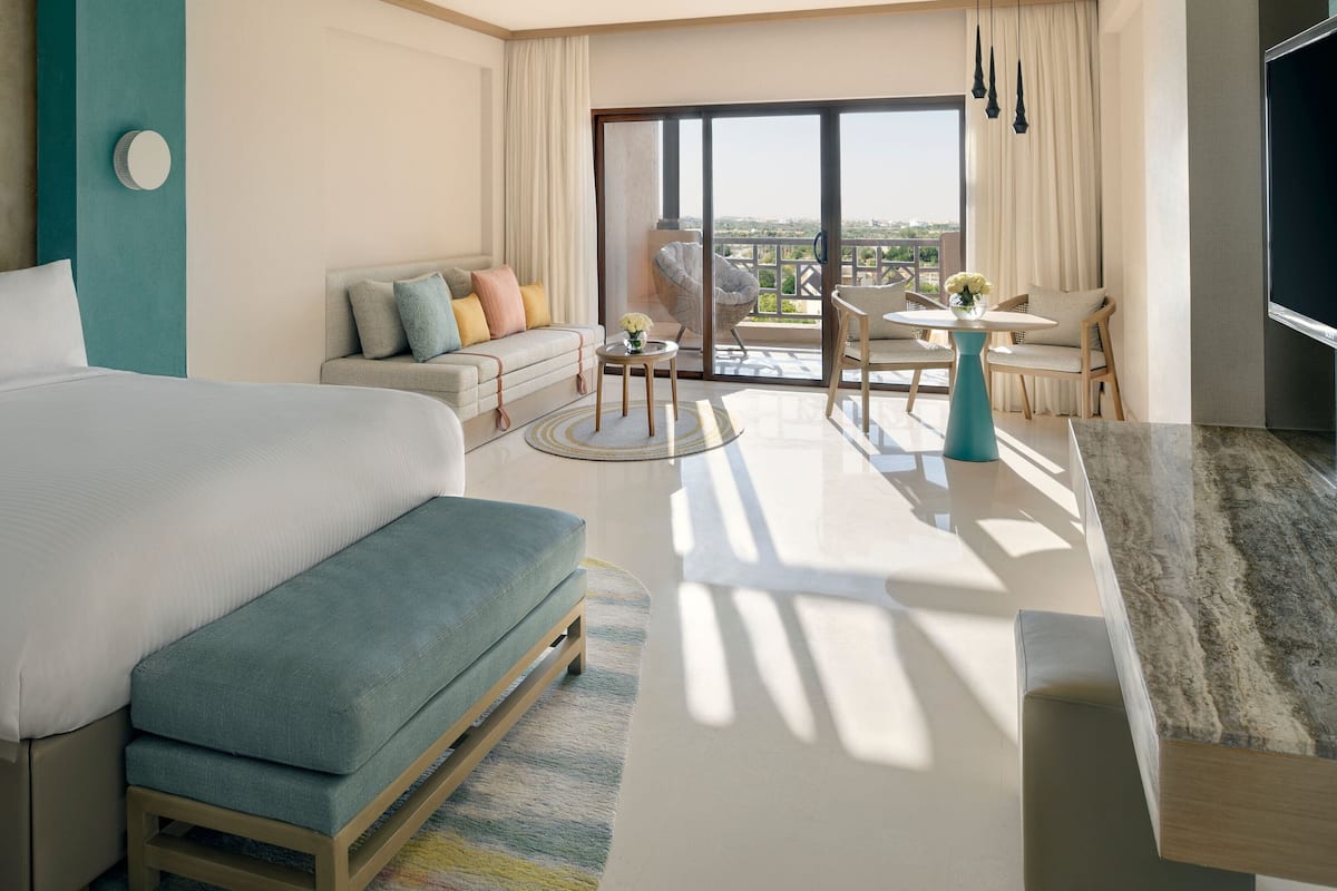 A modern hotel room with a large bed, a sofa, a dining area, and a balcony with a view.