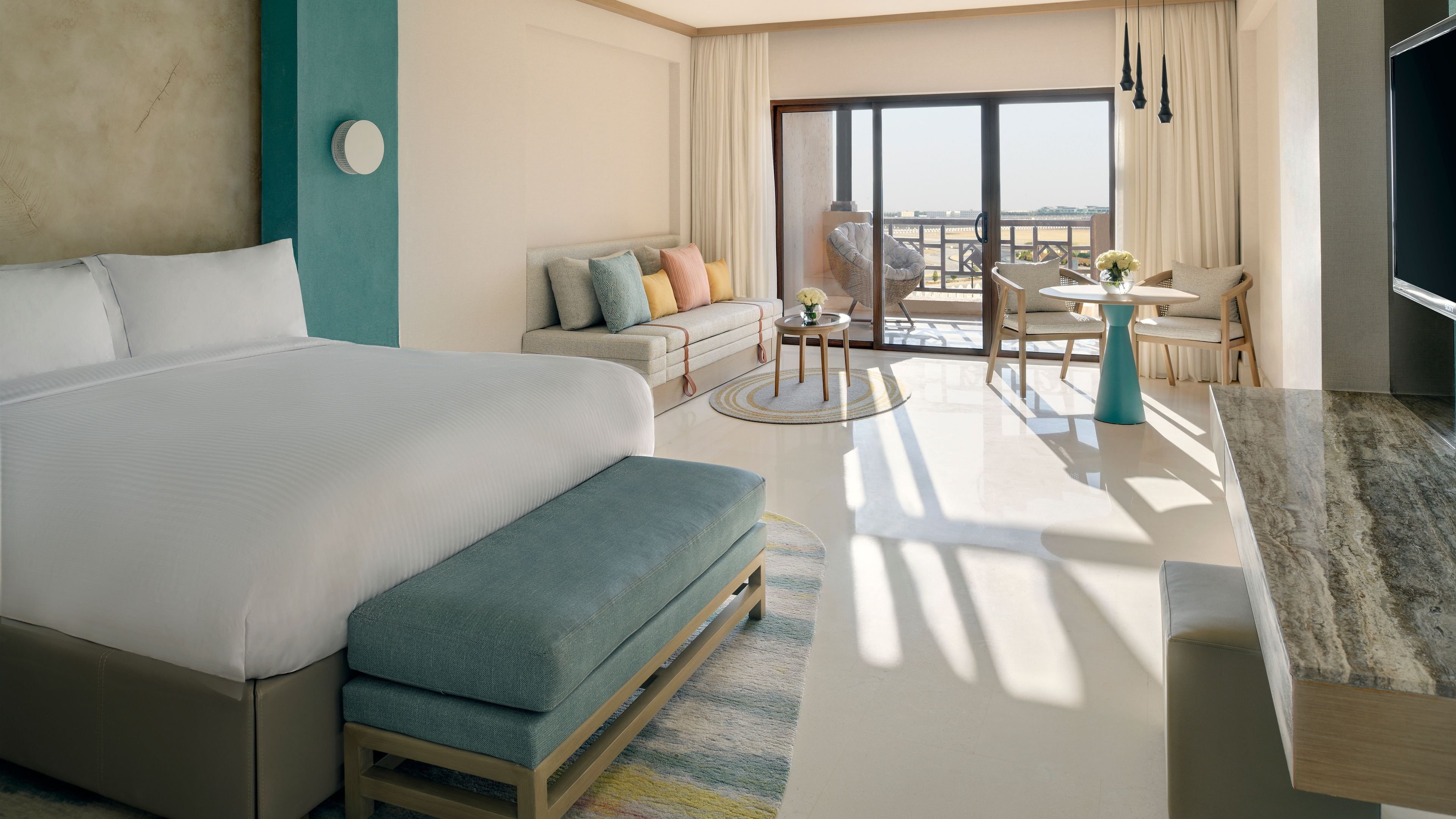 A hotel room with a large bed, a sofa, a dining table, and a balcony with a view.