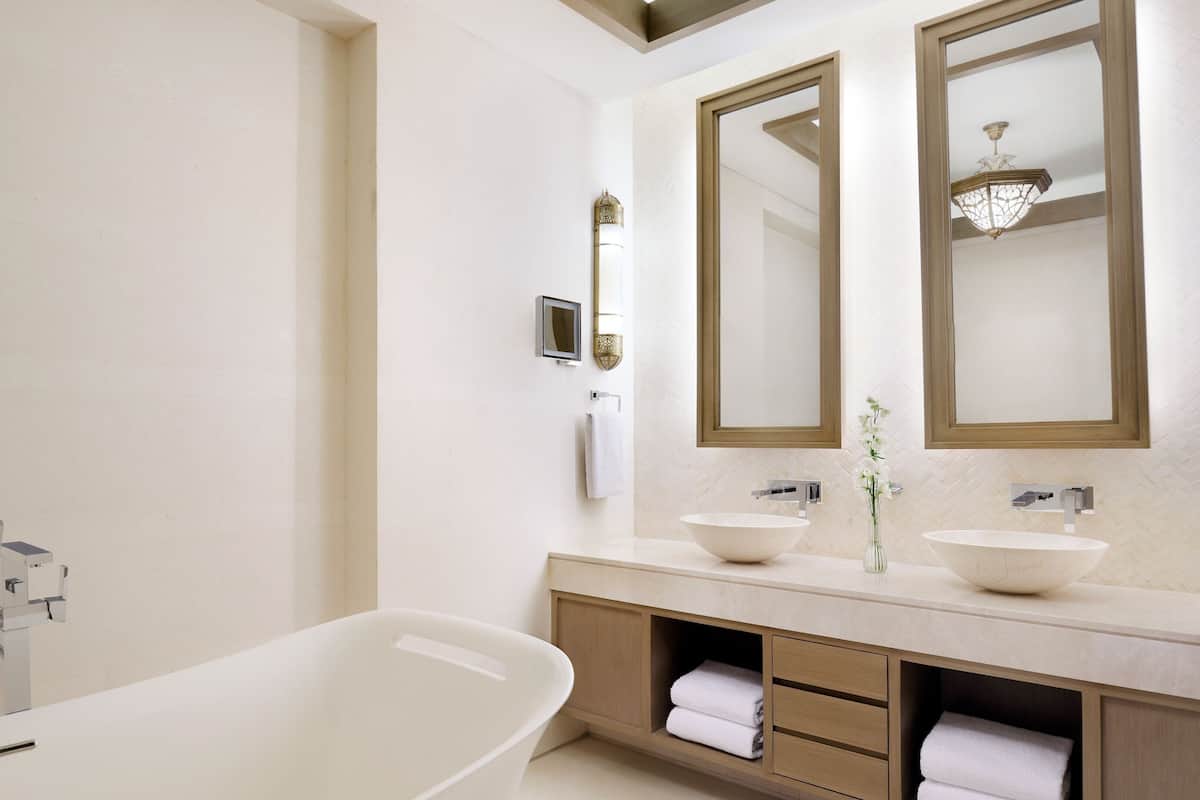 A modern bathroom with a freestanding bathtub, two sinks, and a large mirror.