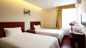 Une chambre d’hôtel avec deux lits simples, un bureau avec une chaise, un radiateur, une fenêtre avec des rideaux et un climatiseur fixé au mur.