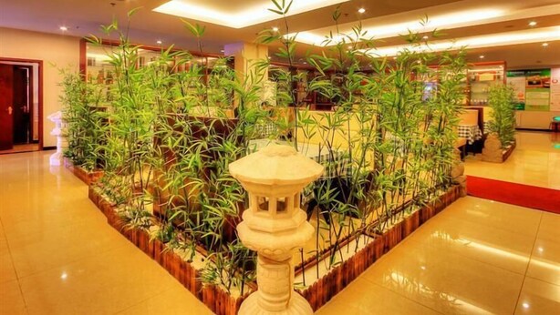 Un hall d’entrée agrémenté d’une fontaine centrale, entourée de plantes de bambou, avec un sol carrelé et un comptoir de réception en arrière-plan.