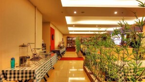 Un restaurant avec de longues tables recouvertes de nappes à carreaux, un sol carrelé et des plantes d’intérieur.