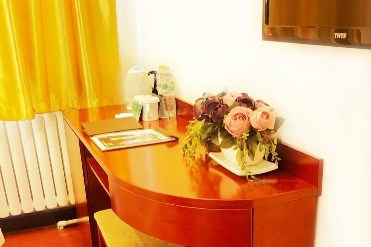 Une chambre d’hôtel avec un bureau en bois, un bouquet de fleurs, une petite table avec une assiette et un radiateur.