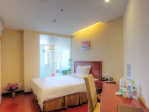 A hotel room with a bed, a chair, a desk, and a small table. There is a window with a view of a building outside.