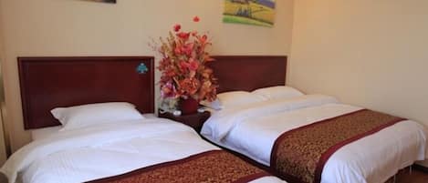A hotel room with two beds, a wooden headboard, a floral centerpiece, and two wall paintings.