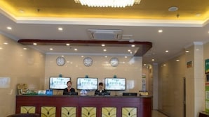 A hotel reception area with a reception desk, three monitors, a clock, and a seating area with a round table and chairs. - Greentree Inn Beijing Yanqing Railway Station (Yanqing)