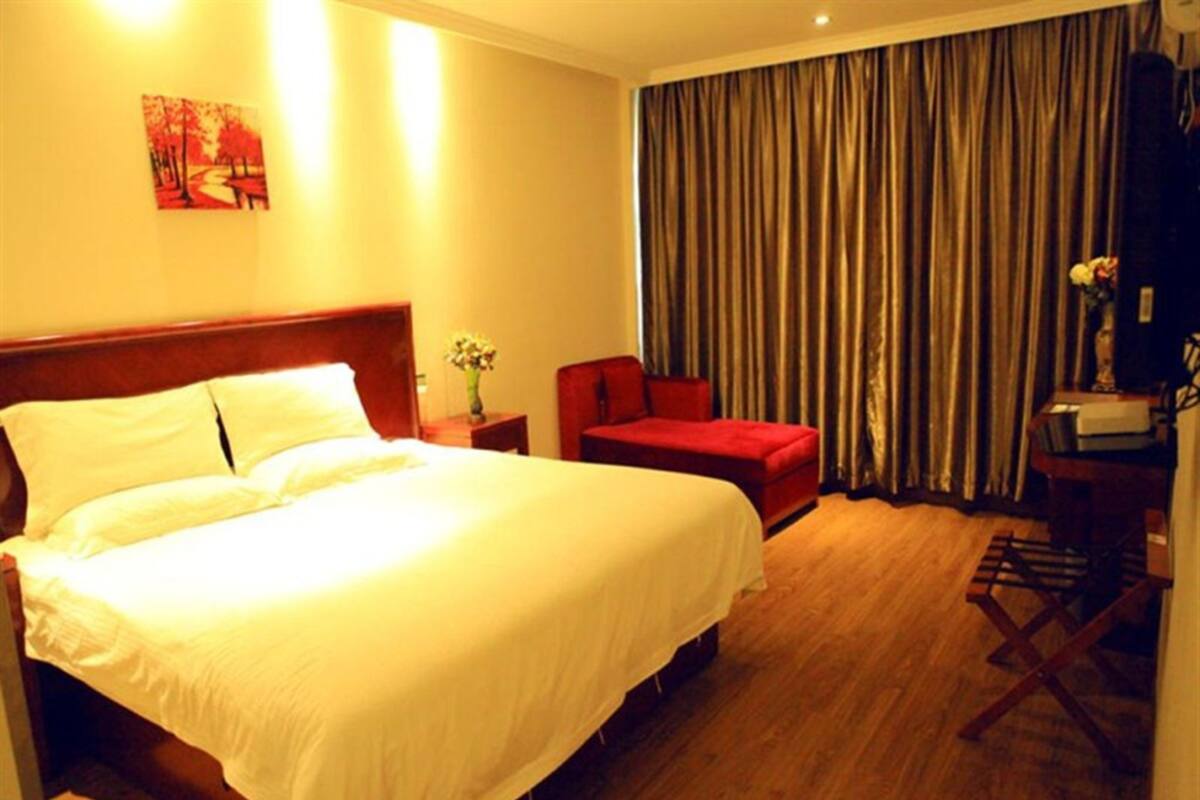 A hotel room with a large bed, a red armchair, a desk with a lamp, and a curtain.