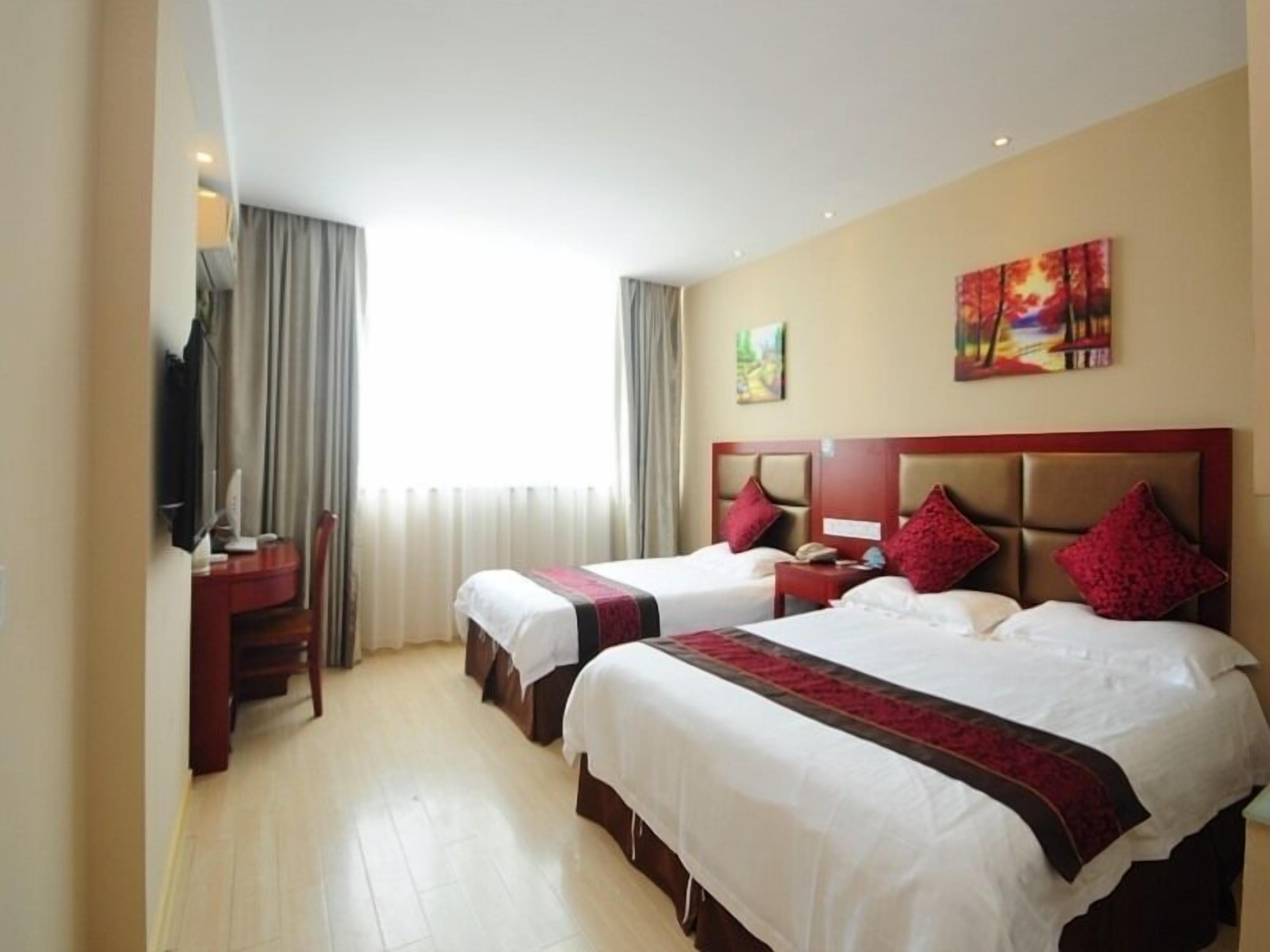 A hotel room with two beds, a desk, and a television.