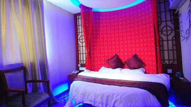 A bedroom with a bed, a chair, and a red accent wall.