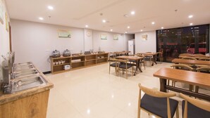A spacious dining area with multiple tables and chairs, a buffet counter with various food items, and a refrigerator in the background. - GreenTree Inn Yancheng Yandu Bus Station Middle Daqing Road Express Hotel (Yancheng)