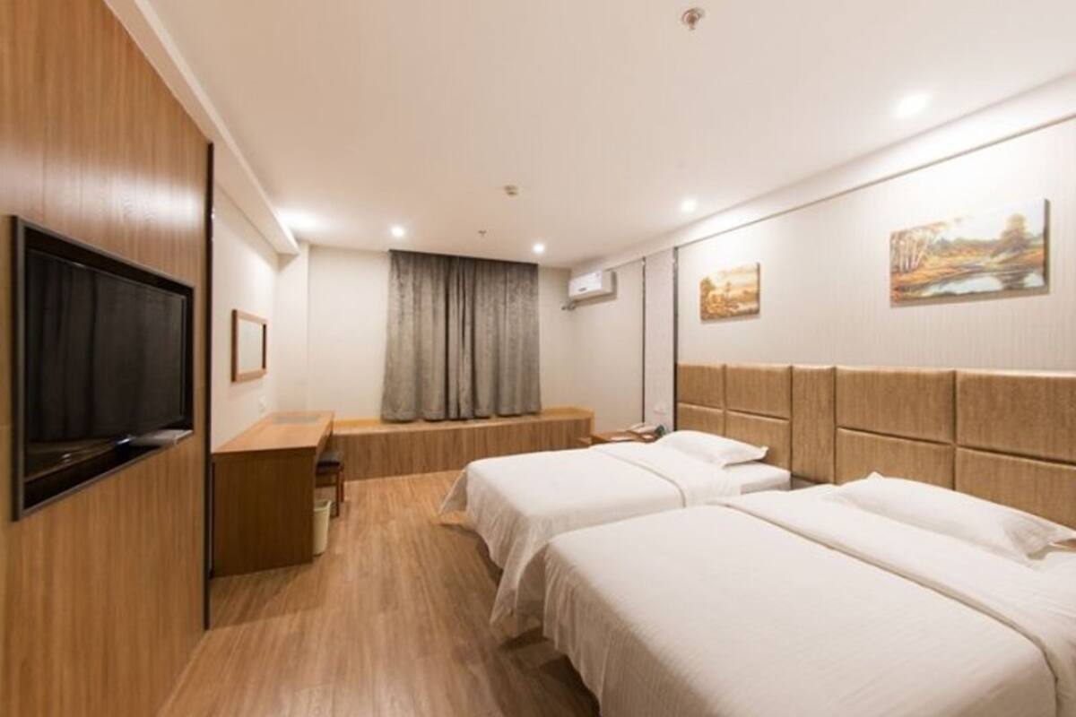 A hotel room with two beds, a TV, a desk, and a window with curtains.