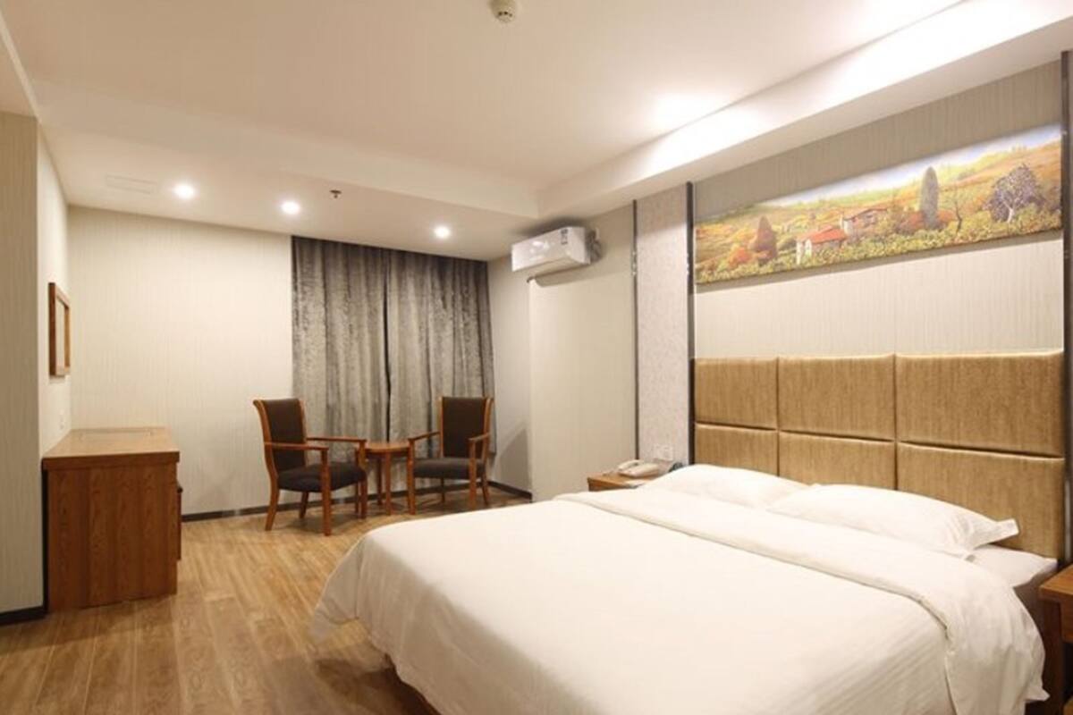 A hotel room with a large bed, a desk, two chairs, and a painting on the wall.