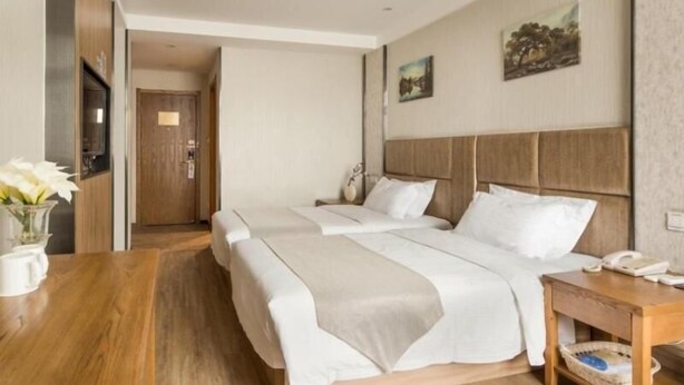 A hotel room with two beds, a wooden nightstand, a vase with flowers, and a painting on the wall. - GreenTree Inn Yancheng Yandu Bus Station Middle Daqing Road Express Hotel (Yancheng)