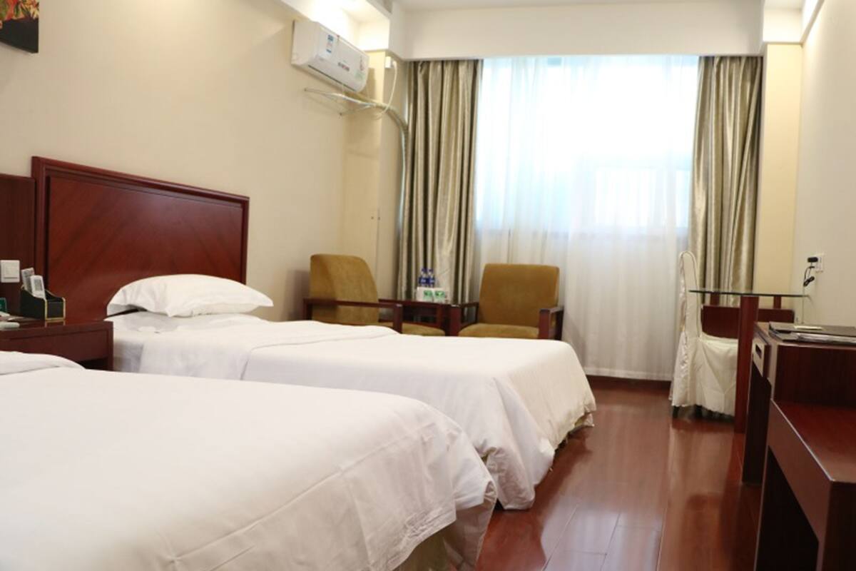 Une chambre d’hôtel avec deux lits, un bureau, une chaise et une fenêtre avec des rideaux.