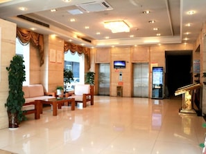A hotel lobby with a reception desk, seating area, and elevators.