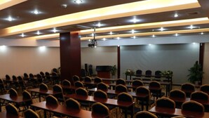 A conference room with rows of tables and chairs, a projector screen, and a stage area.