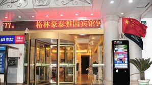A hotel entrance with a revolving door, a 24-hour service sign, and a digital display showing the number 77.