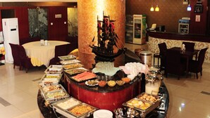 A buffet area with various food stations, a central decorative pillar, and a seating area with tables and chairs.