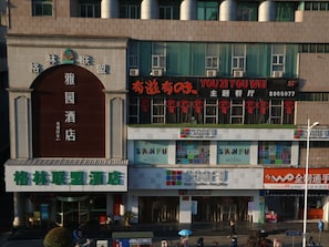 A hotel with a prominent sign reading "雅园酒店" and a large digital display advertising "YOU2YOUWEI".