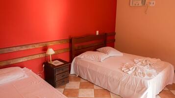 A bedroom with two beds, a wooden headboard, a nightstand with a lamp, and a wall-mounted electrical outlet.