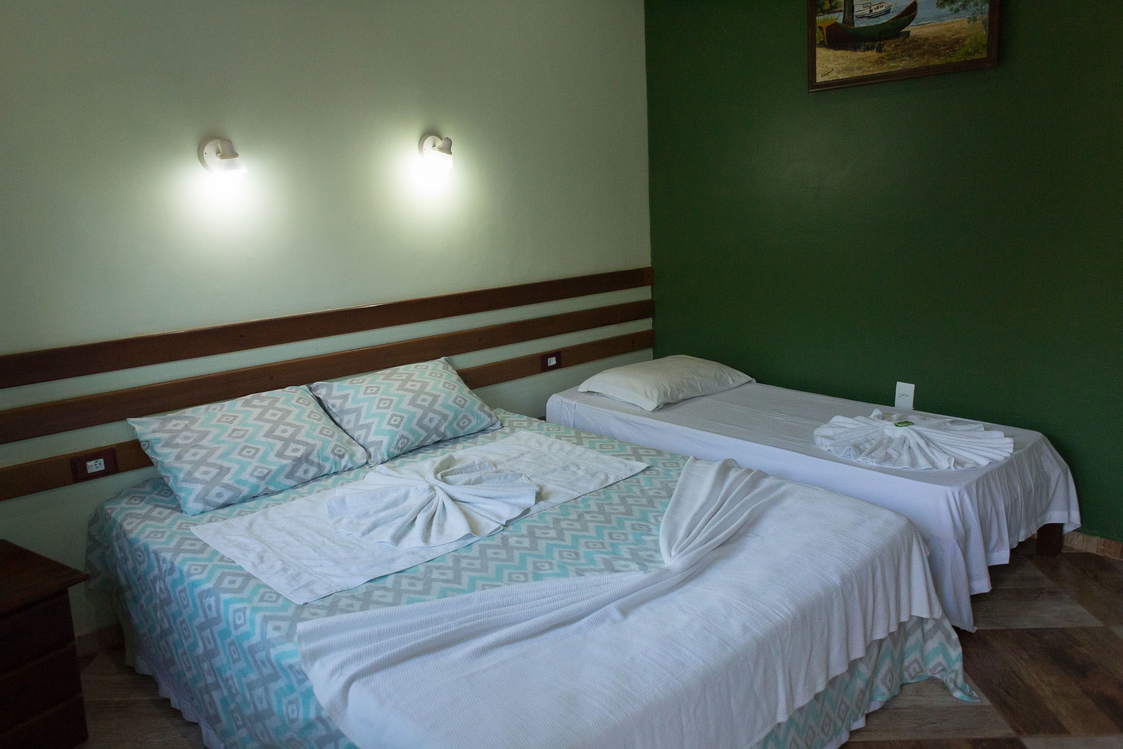 A hotel room with two beds, each with a patterned bedspread and white linens. There are wall-mounted lights above the beds and a painting on the wall.