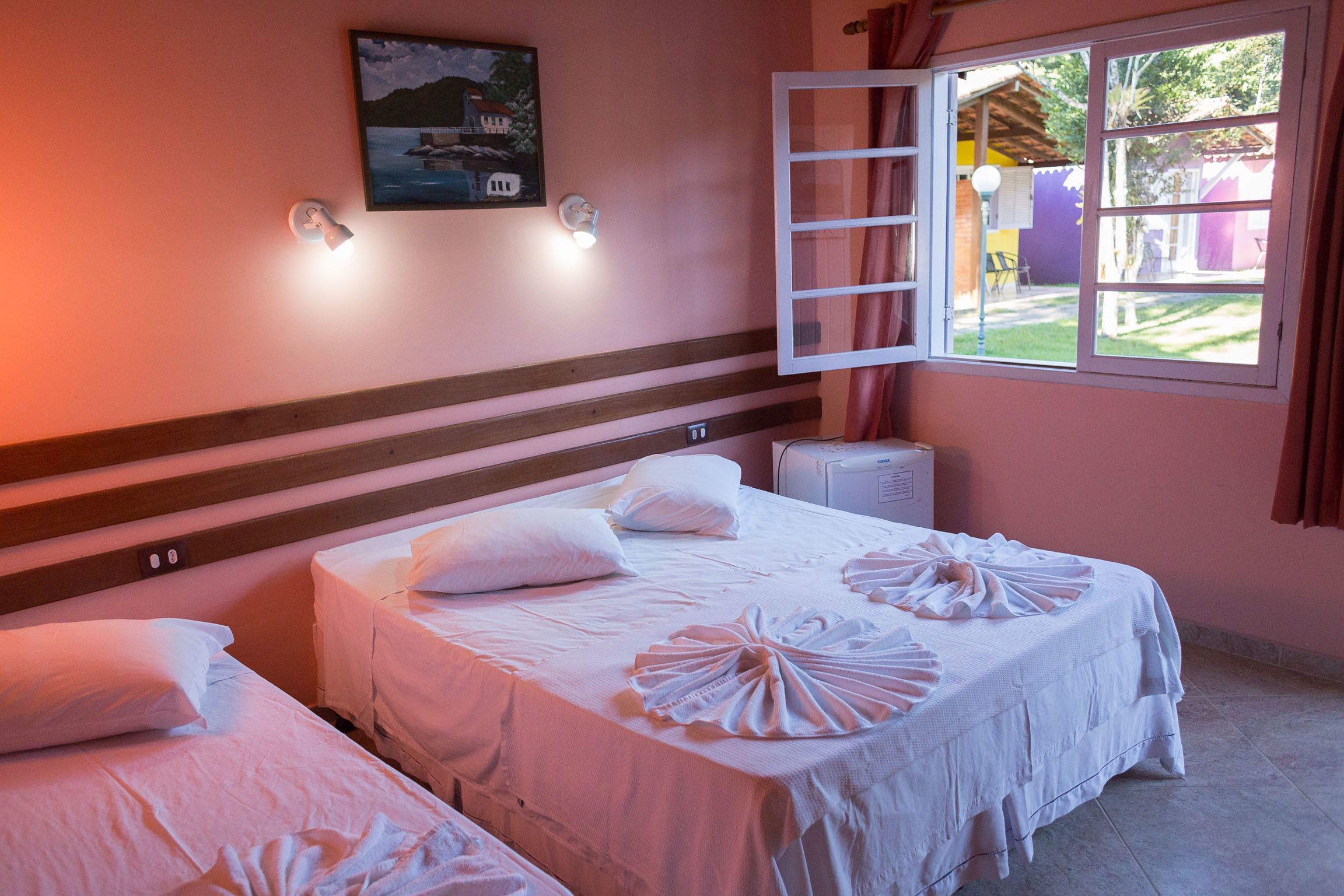 Habitación de hotel con dos camas, un cuadro en la pared, una ventana con cortinas y vistas al exterior.