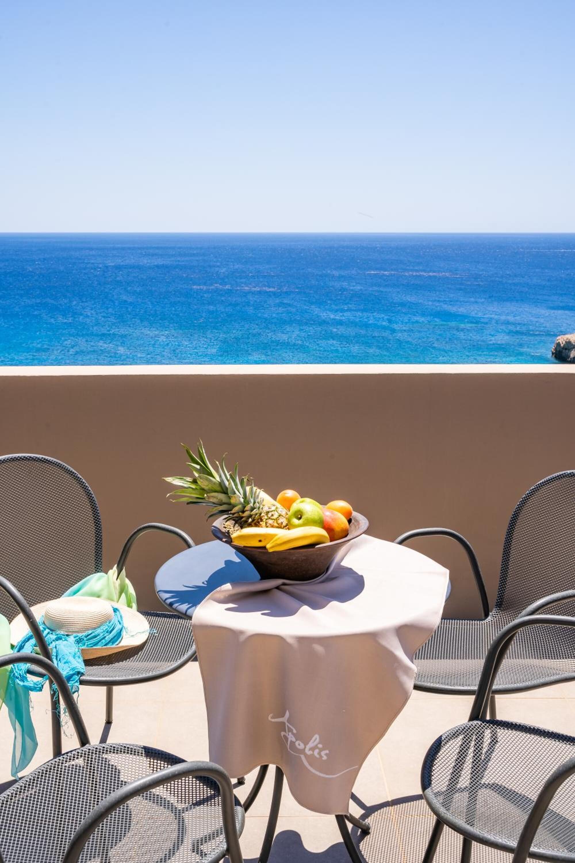 A table with a fruit bowl, chairs, and a view of the ocean.